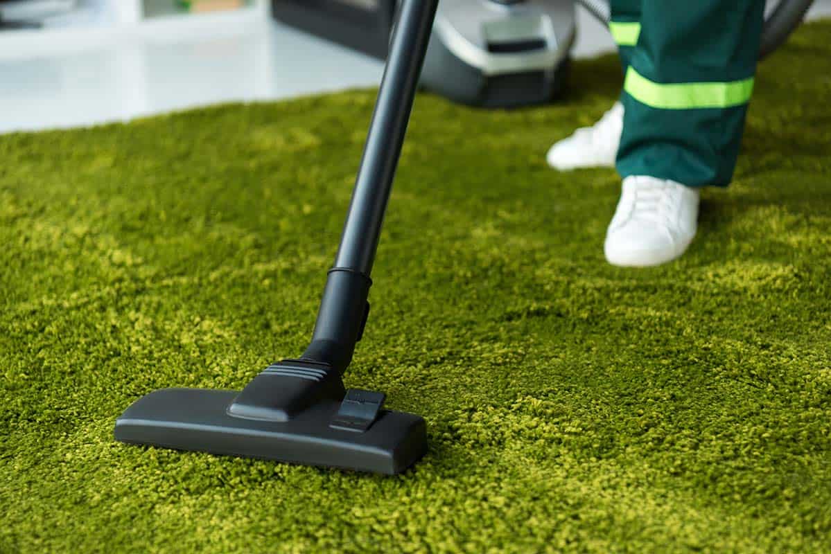 cropped shot of person cleaning green carpet with vacuum cleaner