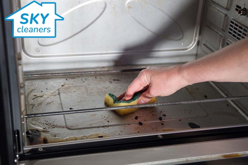 person cleaning a greasy oven on the inside with a sponge